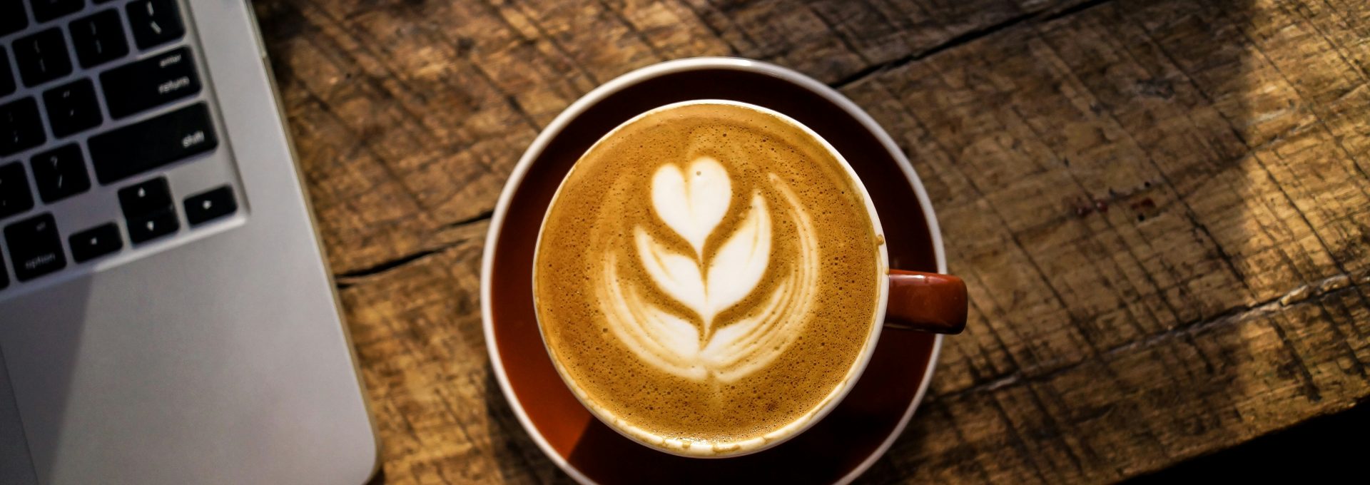 caffe latte on white ceramic cup beside silver and black laptop computer